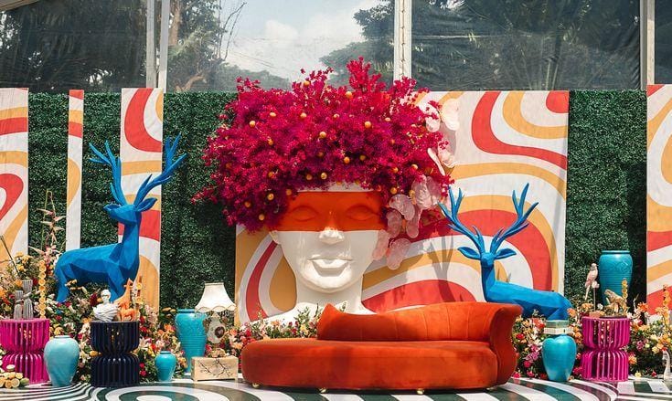 Retro mehendi setup with a bougainvillea face planter and curved orange seating by RAW Group